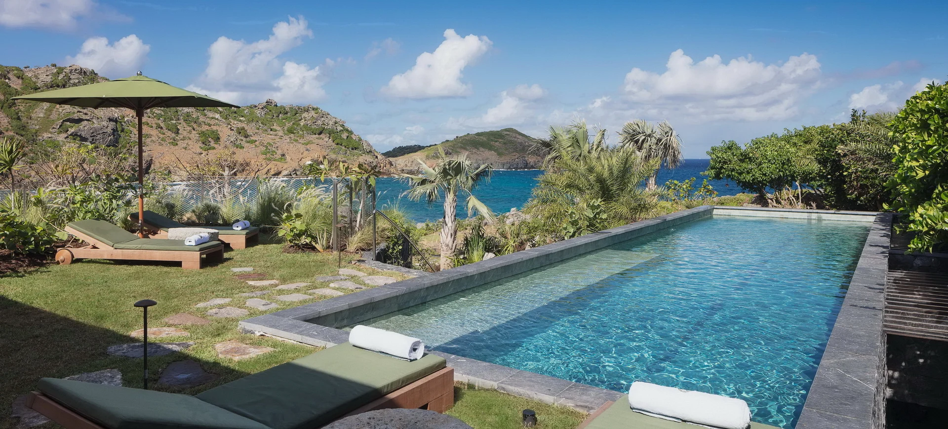 Rectangular pool with lounge chairs and umbrella overlooking ocean and hills at Villa Jangali, Flamands