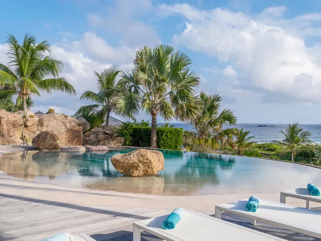 Infinity pool with clear water surrounded by wooden deck and tropical trees at Villa La Roche dans l’Eau, Grand Fond