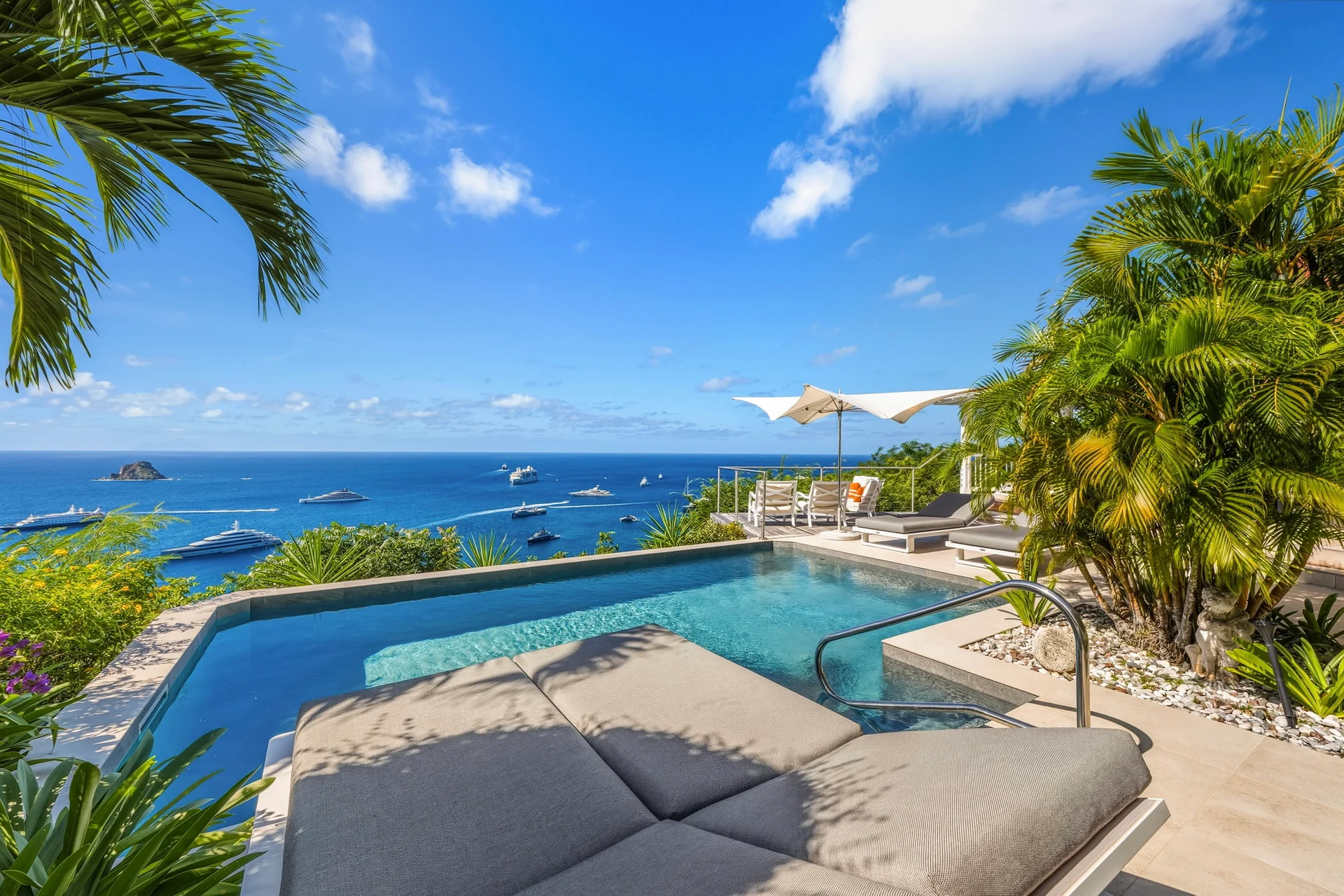 Pool with clear blue water, lounge chairs, umbrella, ocean with boats and island at Villa L’Enclos, Colombier