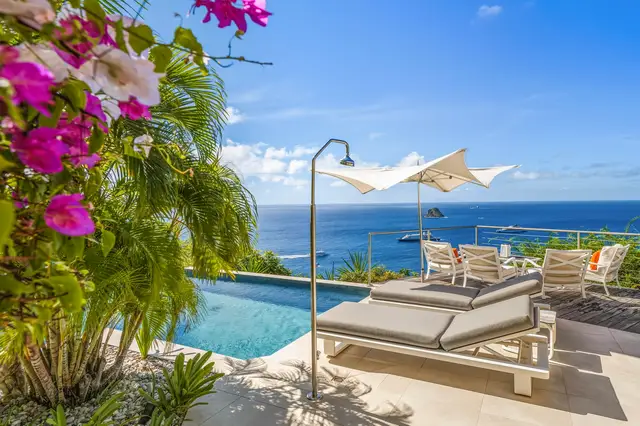 Pool area with lounge chairs, umbrella, shower, ocean view, lush greenery at Villa L’Enclos, Colombier