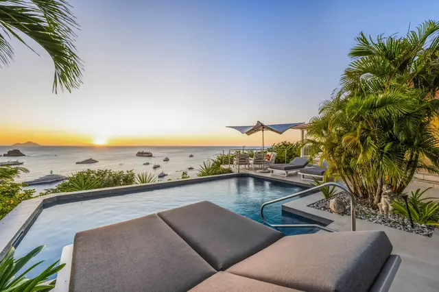 Pool with lounge chairs, umbrella, calm ocean at sunset, boats, tropical plants at Villa L’Enclos, Colombier