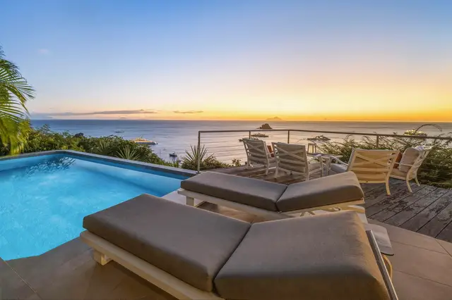 Infinity-edge pool on tiered terrace, lounge chairs, deck, ocean at sunset at Villa L’Enclos, Colombier