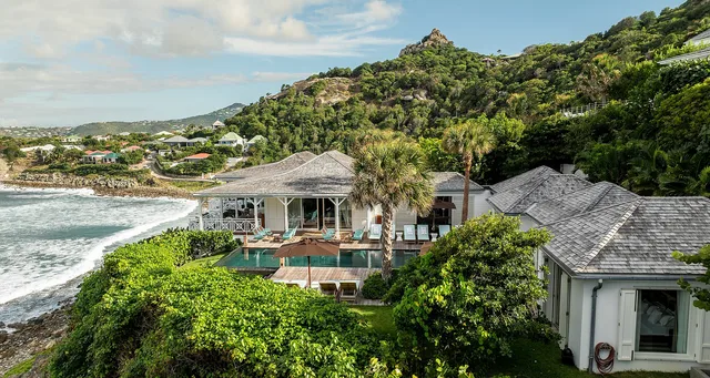 White villa with dark gray roof and pool with turquoise loungers near palm tree at Villa Les Lataniers, Anse des Lezards