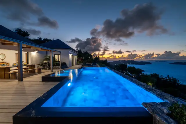 Illuminated infinity pool and dining area with ocean view at dusk at Villa Ma’O, Vitet