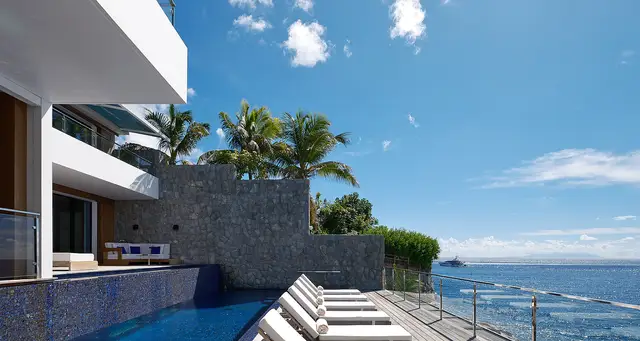 Infinity pool with blue tiles, white lounge chairs on wooden deck at Villa Marlice, Gustavia