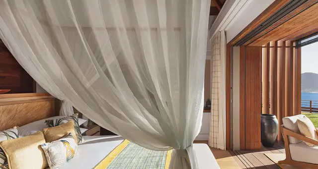 Bedroom with sheer canopy and deck overlooking water and hills at Villa Nougat, Pointe Milou