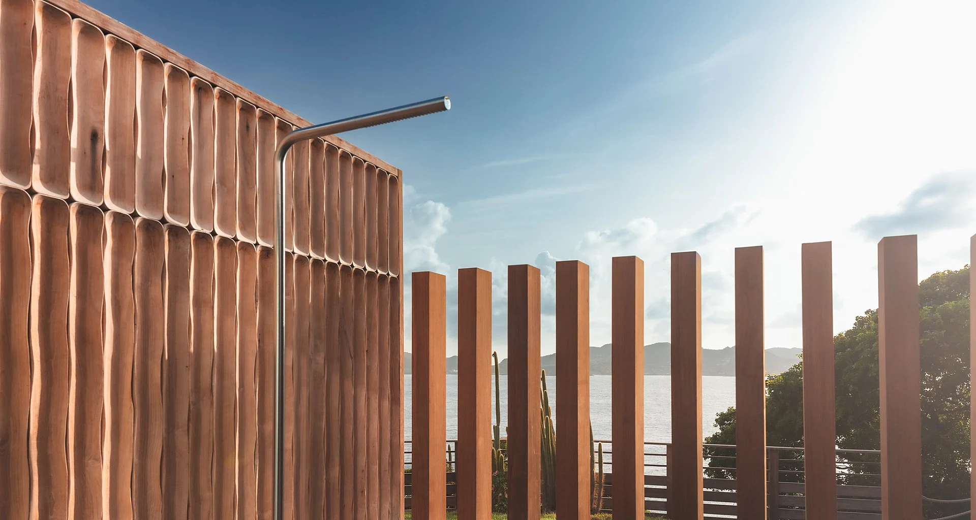 Wooden slat wall with shower head overlooking water and hills at Villa Nougat, Pointe Milou