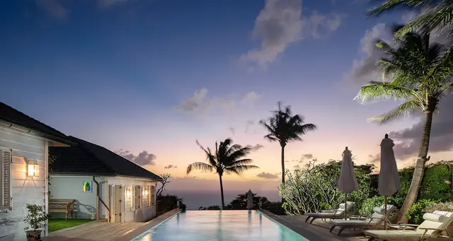 Evening pool with lounge chairs and building lights against twilight sky at Villa Plumbago, Colombier