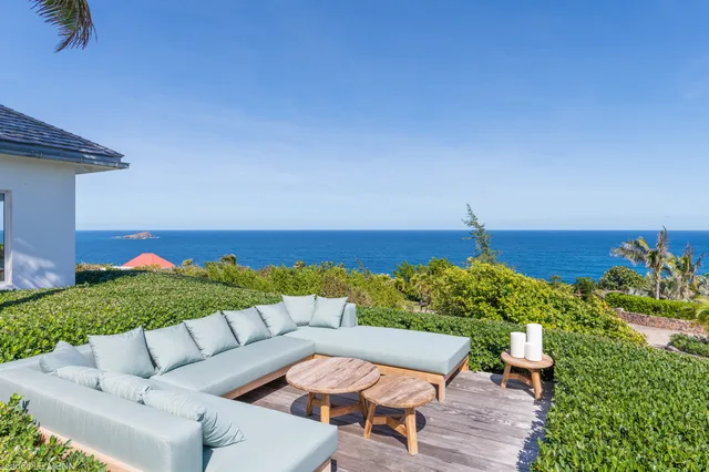 Wooden deck with sofa and tables overlooking ocean and rock formation at Villa Poppy, Mont Jean