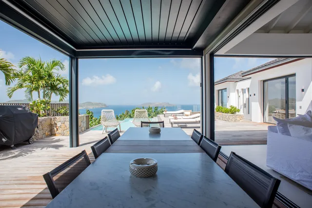 Covered outdoor dining with table and chairs overlooking pool and ocean at Villa Rock, Lorient