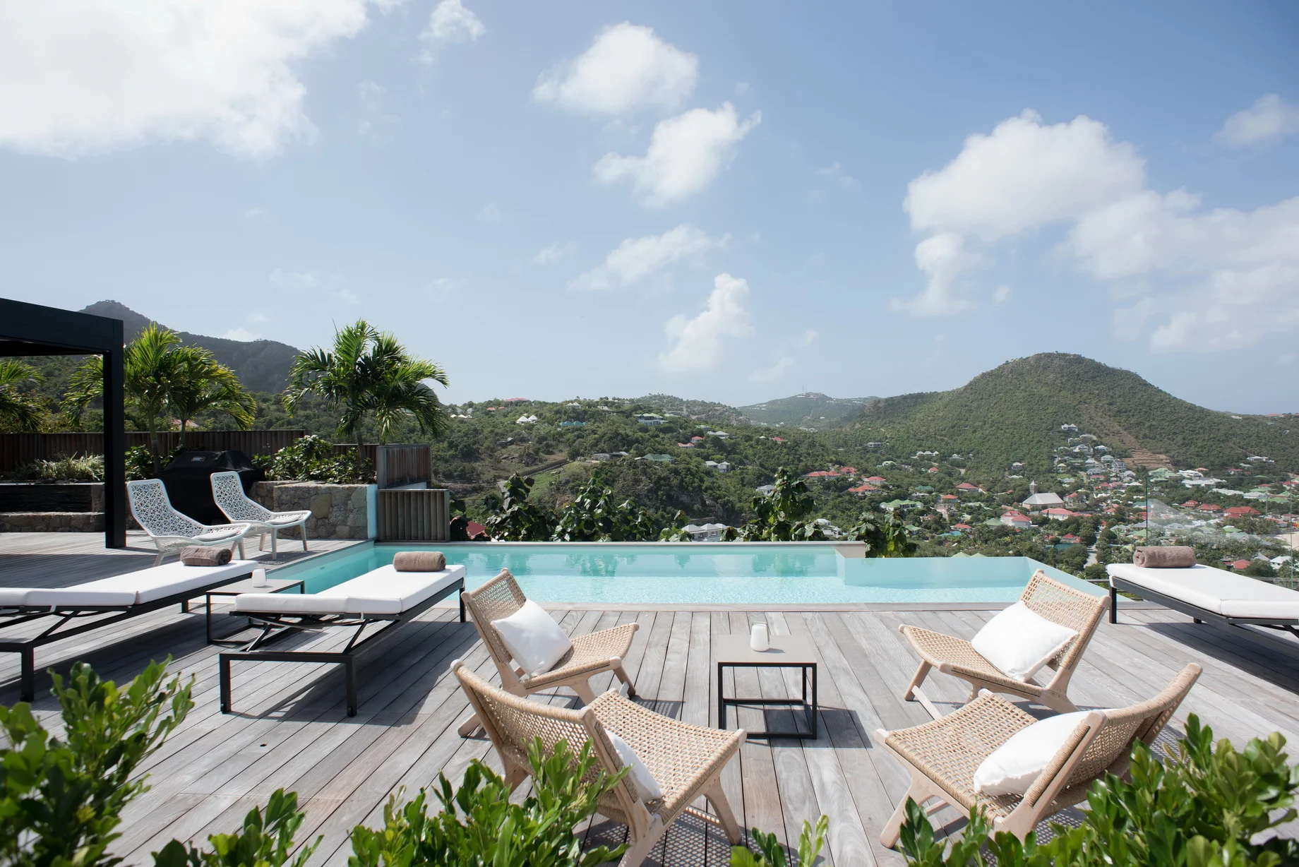 Wooden deck with infinity-edge pool, lounge chairs, valley view with houses at Villa Rock, Lorient